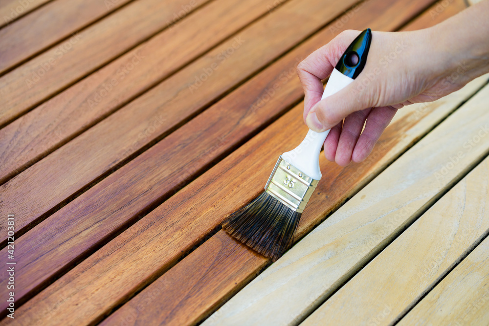 hand holding a brush applying varnish paint on a wooden garden table - painting and caring for wood with oil