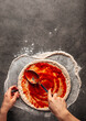 © Hihitetlin - Making a pizza spreding tomato sauce on the dough on the grey concrete background