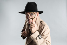 Male Detective With Smoking Pipe Looking Through Magnifying Glass On Grey Background
