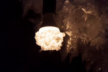 Frozen light bulb, covered with crystal ice and snowflakes, lit in the dark winter background