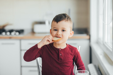 Wall Mural - A child in the afternoon on a white light kitchen in a burgundy sweater eats an omelet