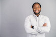 Merry African-American male employee wearing smart casual shirt stands with arms crossed isolated on grey, studio shot of cheerful black businessman, success concept, copy space