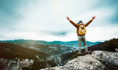 Wall Mural - Man standing on edge of mountain feeling victorious with arms up in the air - Hiker triumph success on the top of the cliff - Success, life goals, achievement concept.