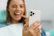 Joyful woman pointing finger at her smile while taking selfie on cellphone