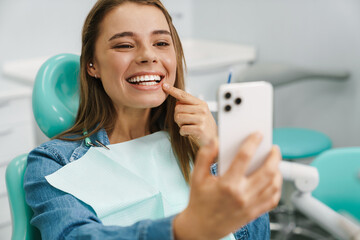 European woman smiling while taking selfie on cellphone at dental clinic