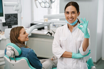 European mid dentist woman showing ok sign while working with patient