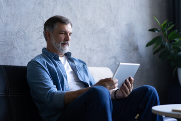 Wall Mural - Mature handsome man websurfing on tablet at home.