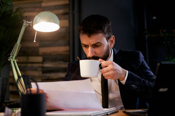 Wall Mural - Young businessman drinking coffee in his office. Businessman drinking coffee while working late.