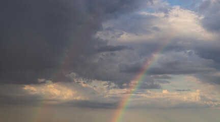 Wall Mural - rainbow on dramatic dark sky with rays and white clouds
