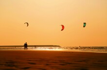 Kites Flying Over Sandy Beach At Sunset