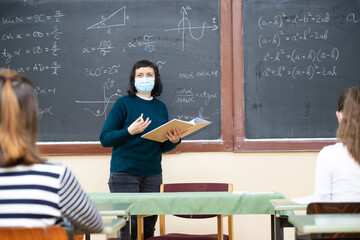 Students in protective face masks studying in classroom with teacher. Precautions in coronavirus pandemic
