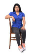 © Curto - front view of full portrait of a latin woman dressed in jeans sneakers and shirt sitting on chair on white background