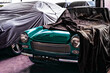Italienischer grüner Oldtimer-Sportwagen. Bis zur Motorhaube mit Tuch bedeckt. Steht neben anderen abgedeckten Oldtimern in Garage