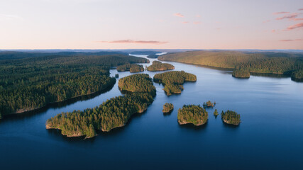 Wall Mural - Aerial view of small islands on a blue lake at sunset. Birds eye view of scenic lake surrounded by green forest.