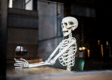 Human Skeleton Bones Sat In Leather Chair In Pub Holding A Glass Of Alcohol Wine Waiting A Long Time For Pubs And Bars To Re-open After Being Closed During Covid-19 Coronavirus Pandemic Lockdown