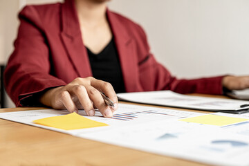 A close-up of a business woman holding a pen and examining the monthly sales document summarized by the sales department, she is analyzing and planning to increase sales. Sales management concept.