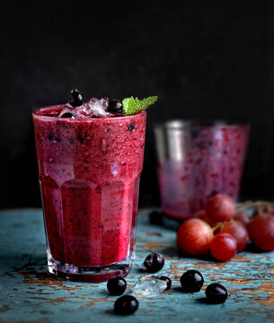 grape and black currant smoothie in transparent glass front view on old wooden blue table on dark background closeup. Selective focus