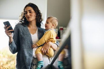 woman holding her baby and texting on her phone