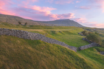 Wall Mural - Vibrant, colourful sunrise or sunset sky over the beautiful countryside landscape of limestone pavement old stone walls at Southerscales in the Yorkshire Dales National Park, UK.