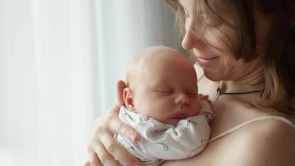 mother holding a newborn baby in her arms. young mother is keeping in arms and caressing her newborn