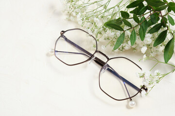 stylish glasses and flowers on a light background copy space, optics, a fresh twig with leaves and small white flowers for a spring mood