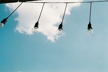 Low Angle View Of Light Bulbs Hanging Against Blue Sky