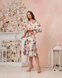 Fashion female model in white sun dress with floral print standing and posing in pink room