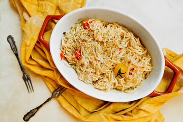 trendy vegan healthy food. pasta from feta cheese with small tomatoes in olive oil with herbs and spices in ceramic baking dish with yellow cotton napkin. step-by-step recipe, step 3. selective focus