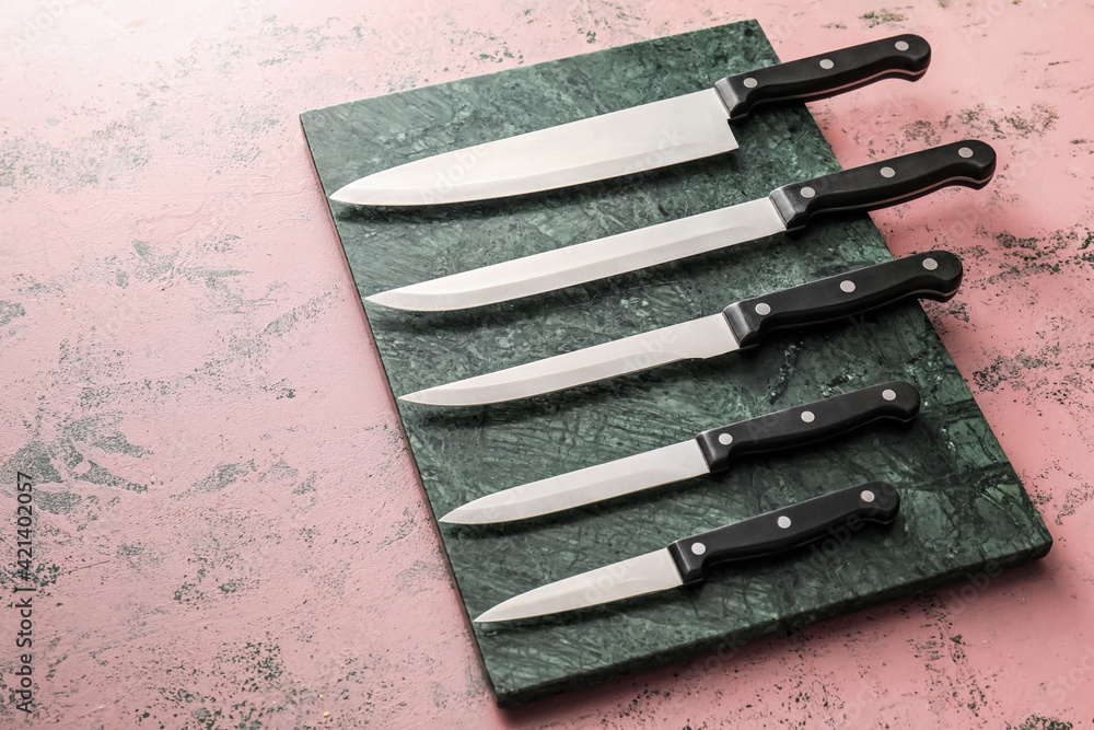 Board with set of knives on color background