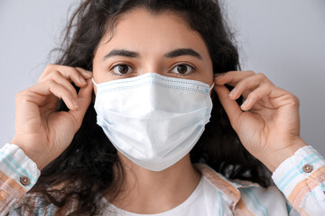 Young woman wearing medical mask on grey background