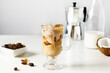 Iced coffee with coconut milk in a tall glass on white wooden table. Cold refreshment summer coffee drink.