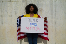 African-american Woman Holds A Black Lives Matter In Her Hands And United States Flag Over Her Shoulder. In Background Grey Wall