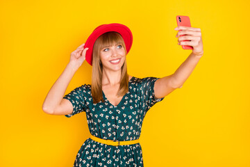 Sticker - Portrait of charming cheerful girl taking selfie posing touching hat having fun isolated over bright yellow color background