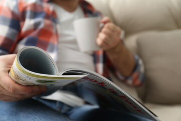 Poster - Man with cup of drink reading magazine on sofa, closeup