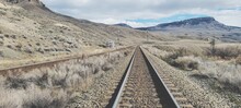 Railroad Track Leading Towards Mountain Range Against Sky