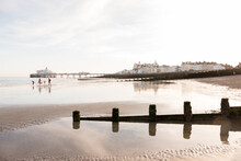 Low Tide On A Wet Sandy Beach With Wooden Groyne In The Foreground And Buildings In The Background