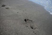 foot prints on a black sand beach with tilt-shift blur. Surf in background.