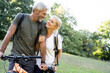© PhotoAlto - Smiling mature couple with bicycle looking at each other in forest