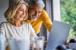 © PhotoAlto - Smiling mature couple using laptop at home