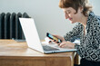© PhotoAlto - Smiling woman using smartphone and laptop while working from home