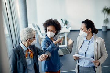 Wall Mural - Happy businesswomen with face masks elbow bumping while greeting in the office.