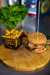 Poster - High-angle shot of a big burger and french fries served on a wooden board in a cafe