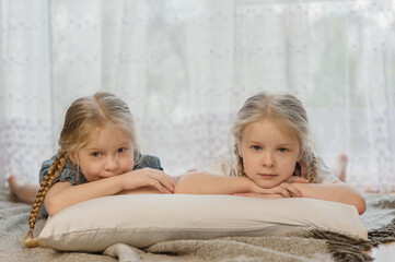 two little girls sisters lie on their stomachs on the floor at home and smile