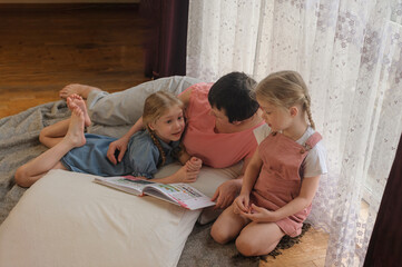 grandmother reads a book to two granddaughters at home