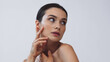 © LIGHTFIELD STUDIOS - brunette woman with perfect skin touching face while looking away isolated on grey