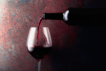 Red wine is poured from a bottle into a wine glass on rusty brown background.