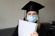 © Iryna - A student in mask is wearing a graduation cape and robe holding blank copy space place concept of the class of 2021 coronavirus pandemic of the covid. Graduation student on white background
