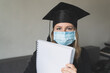 © Iryna - A student in mask is wearing a graduation cape and robe holding blank copy space place concept of the class of 2021 coronavirus pandemic of the covid. Graduation student on white background