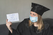© Iryna - Graduate girl in medical mask at coronavirus covid-19 period. Woman with master degree in black graduation gown and cap. Distance learning online. Study at home. Graduation from college.