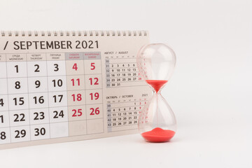 Time passing concept. Crystal hourglass with red sand and calendar on light background